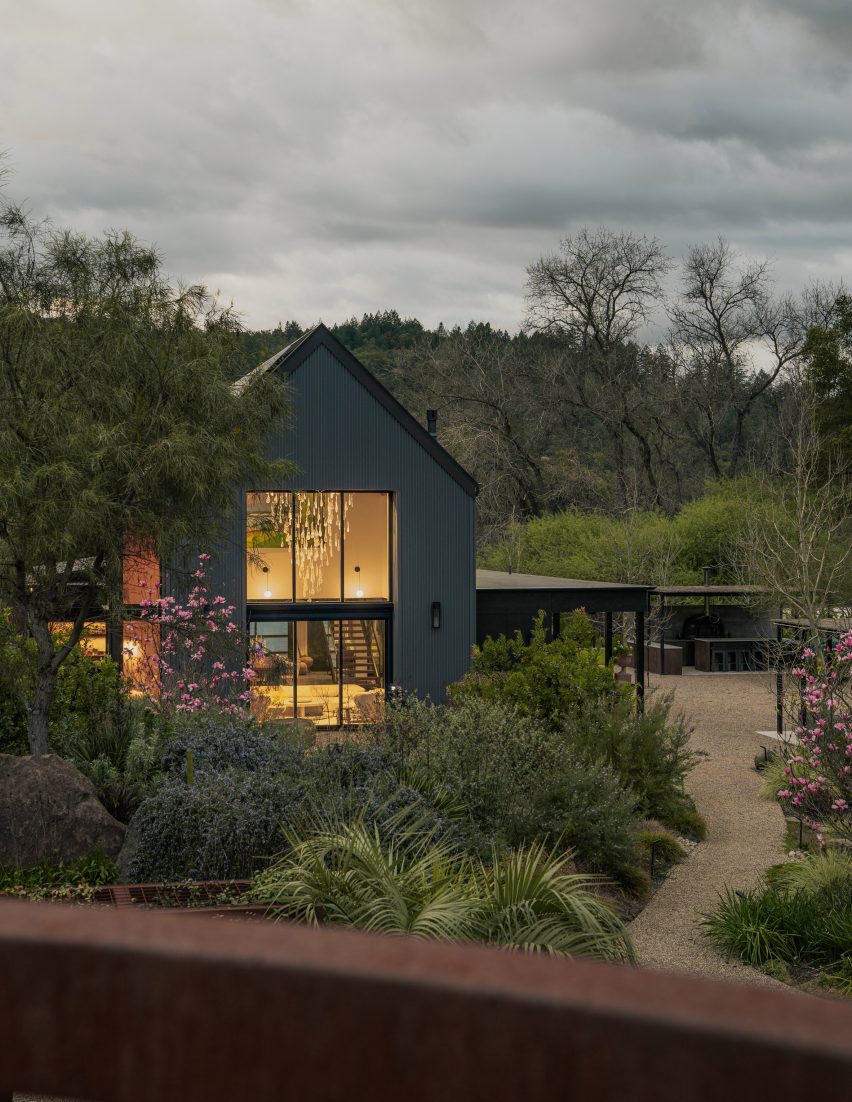 Dark-clad house with a double-height glazed living room overlooking a landscaped garden