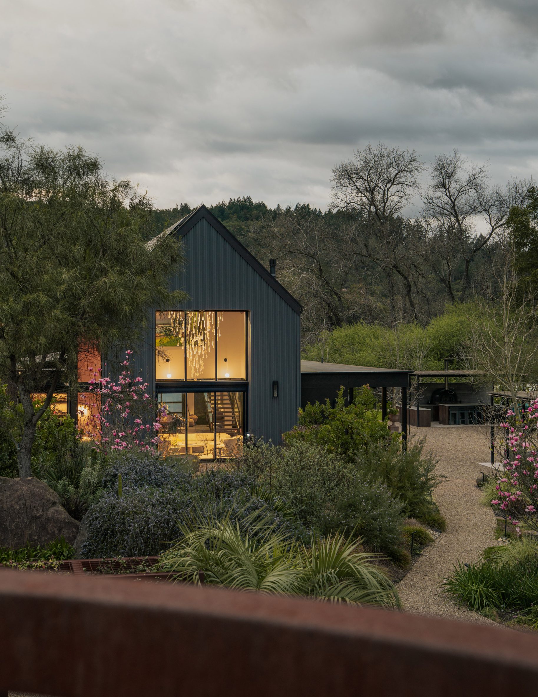 Dark-clad house with a double-height glazed living room overlooking a landscaped garden
