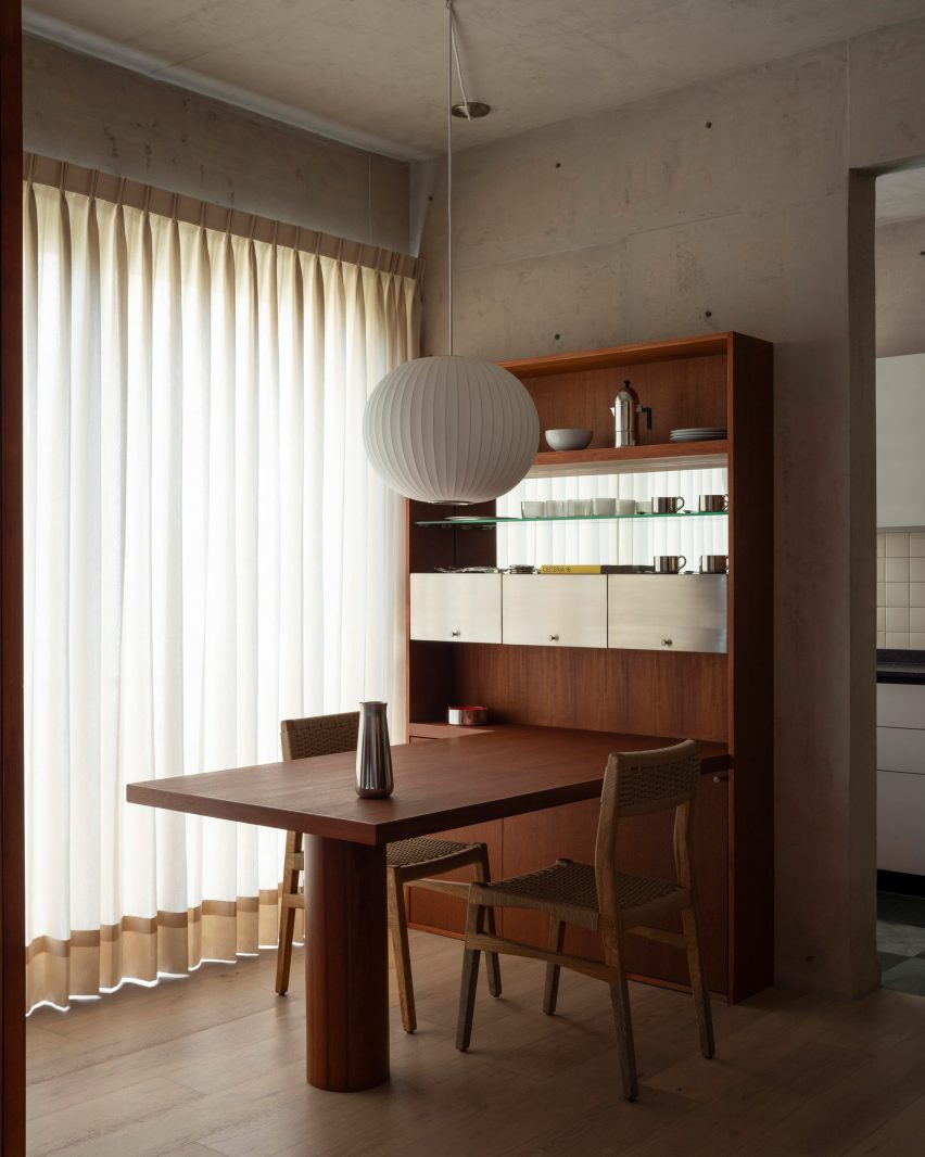 A bespoke teak wood dining table and shelves within a concrete interior