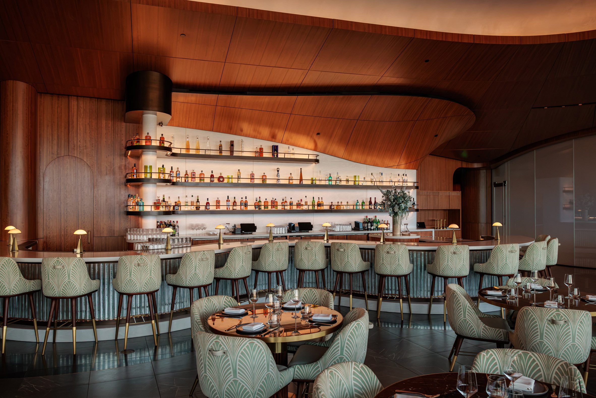 Shimmering tiles cover the front of a snaking bar, while the back bar is clad in illuminated Corian
