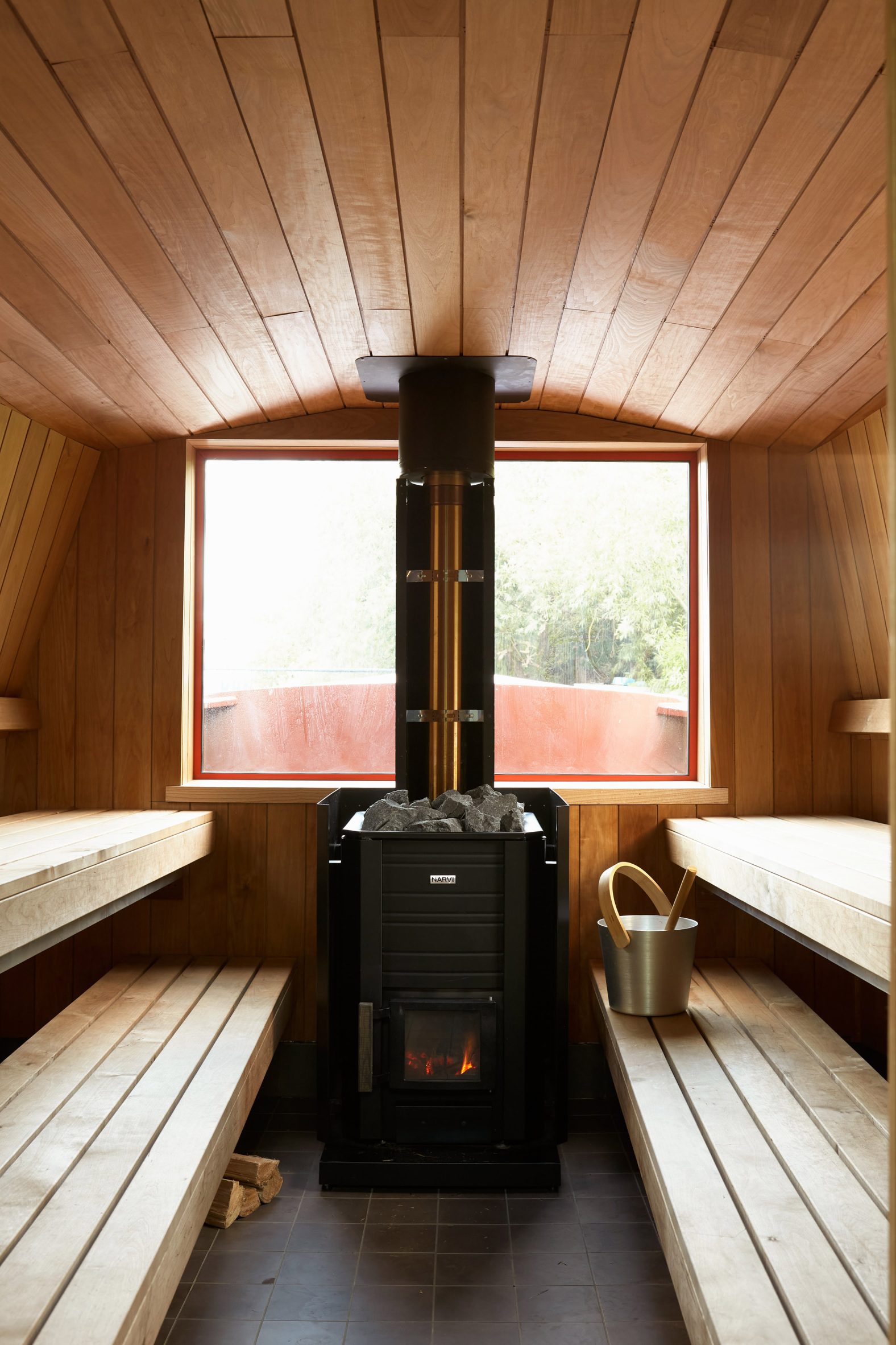 Timber-lined sauna with a wood-burning stove between two levels of benches