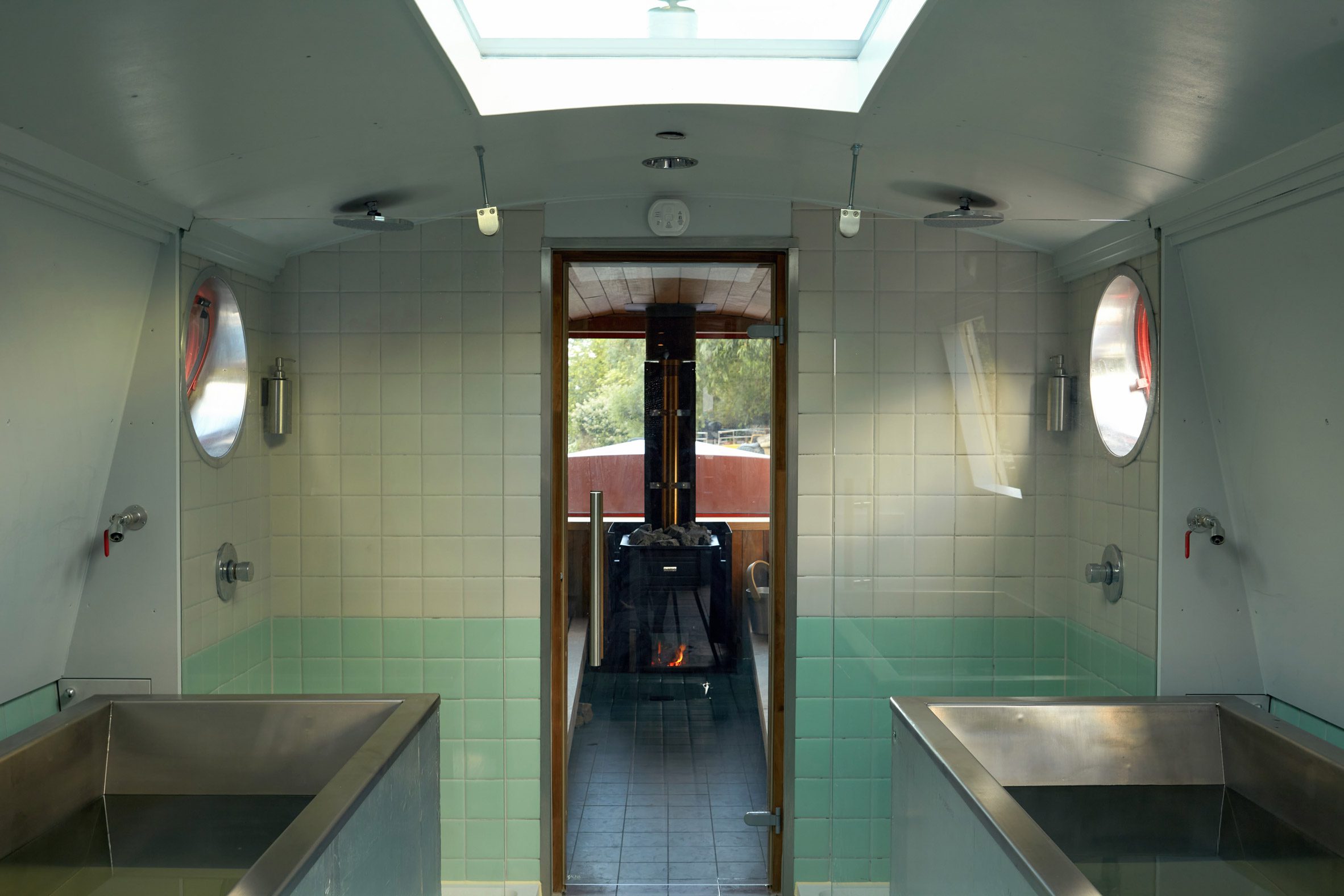 Two stainless-steel plunge pools in a pale green tiled room beneath a skylight