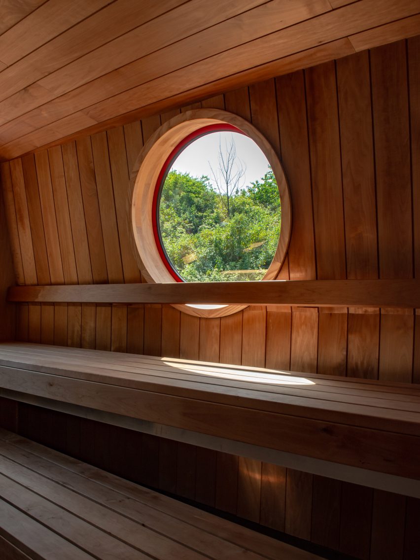 Timber sauna bench beneath a circular porthole overlooking trees