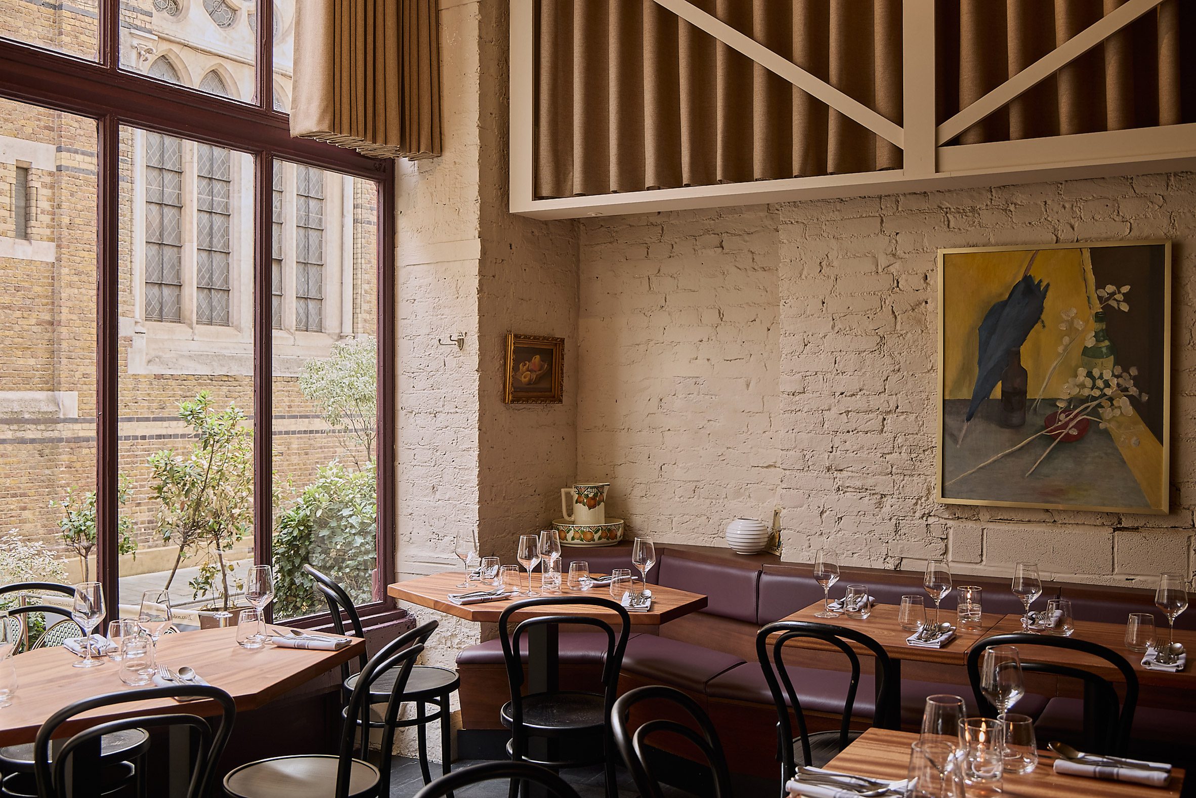 Photograph of the restaurant interior with exposed brickwork, and a glimpse of the glass facade. There is a large piece of artwork on the wall.