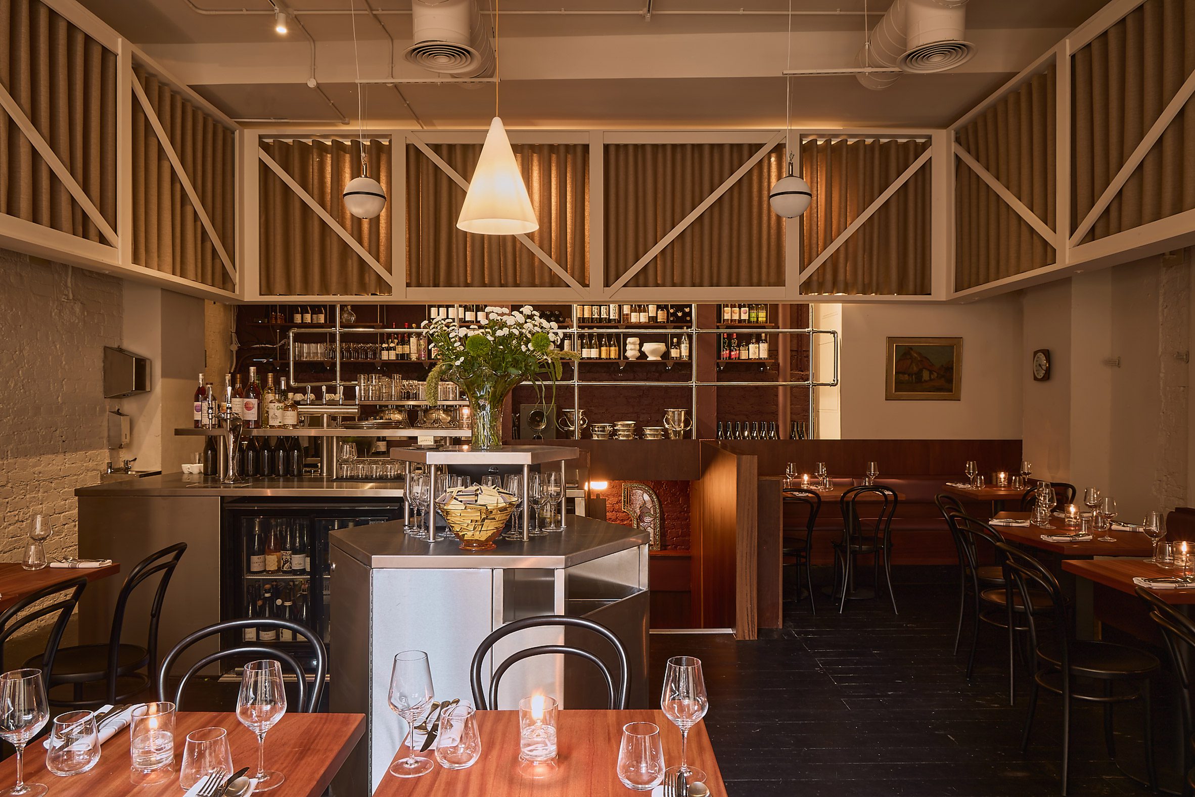 Photograph of a restaurant interior with wooden tables, a wrap-around curtain at the top of the room and stainless steel bar islands.