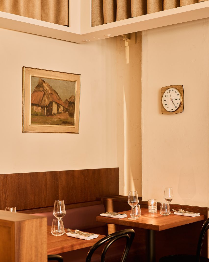 Photograph of a small corner of the restaurant with cream walls, dark-wood banquette seating and wooden tables