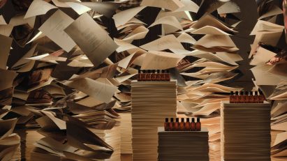 Aesop fragrance bottles displayed on stacks of books beneath suspended paper sheets