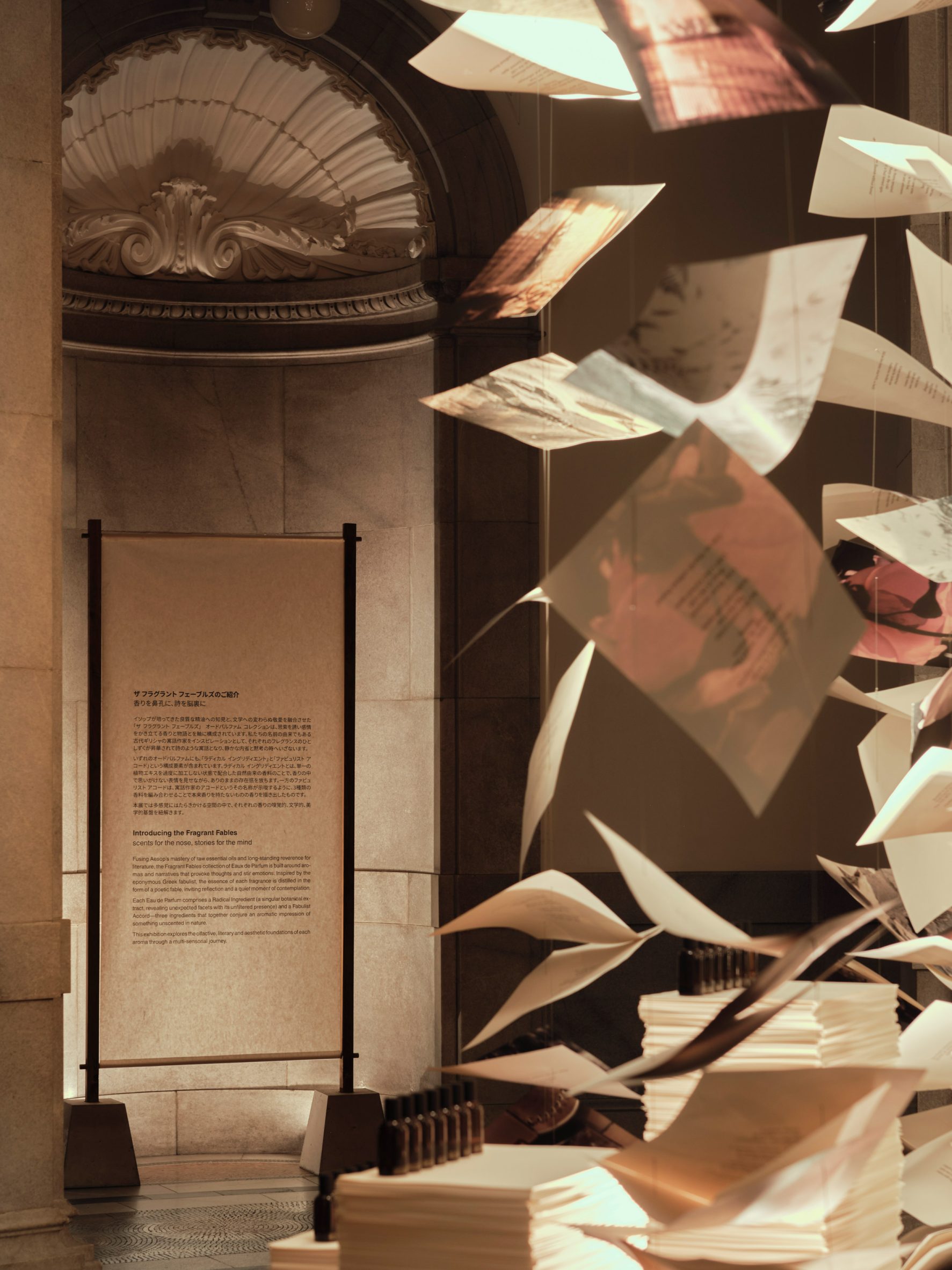 Printed paper sheets and fragrance bottles suspended beside a museum display
