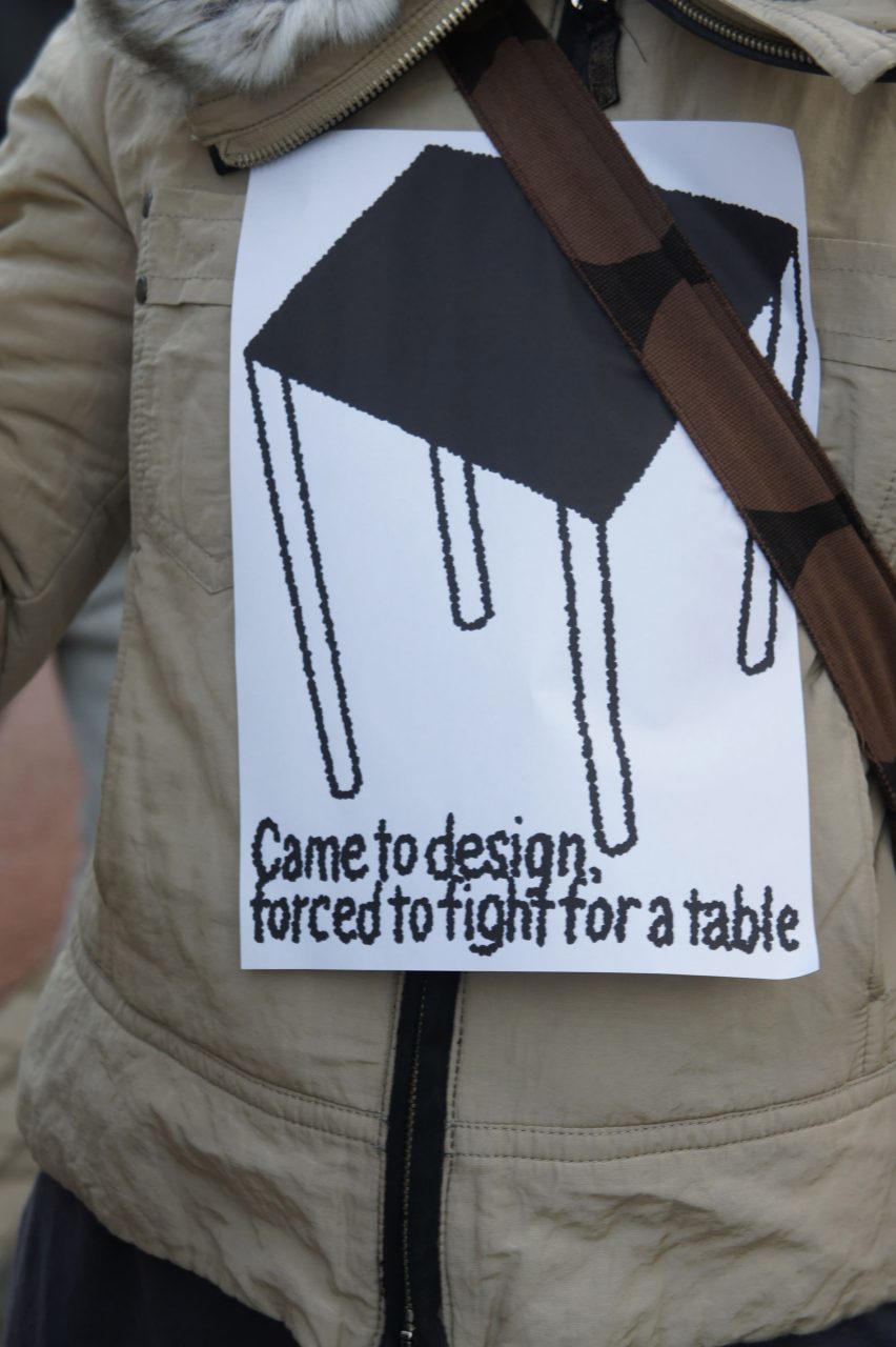 Close-up photo of a protest sign stuck to a person's jacket reading Came to design, forced to fight for a table