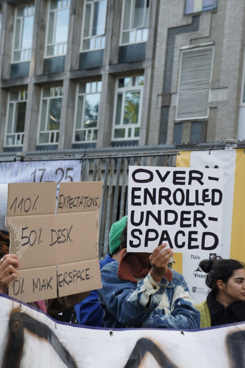 Photo of a protest at the Design Academy Eindhoven with signs reading 110% expectations, 50% desk, 0% makerspace and over-enrolled under-spaced